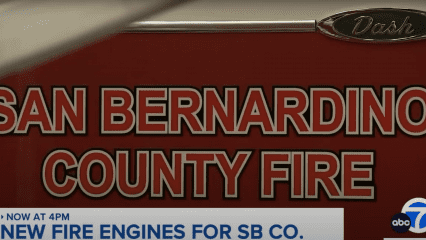 Close-up image of the side of a red fire engine with bold white and black lettering that reads “SAN BERNARDINO COUNTY FIRE.” A metallic emblem labeled “Dash” is visible at the top. In the bottom corner, a news banner from ABC7 reads: “NOW AT 4PM – NEW FIRE ENGINES FOR SB CO.” The image highlights a news segment about newly acquired fire engines for San Bernardino County Fire Department.